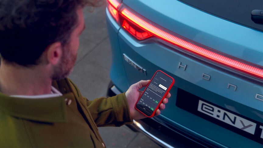 Dáma stojící vedle bílého vozidla Honda e používající aplikaci My Honda+