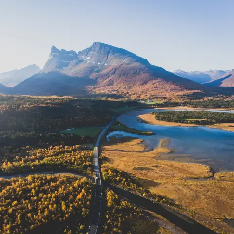 Klasický skandinávský pohled na horskou krajinu se silnicí, horami a fjordem s modrou oblohou v létě, severní Norsko, kraj Finnmark, záběr z dronu